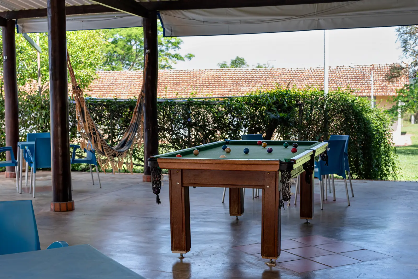 Mesa de sinuca na área coberta, com redes e o jardim ao fundo