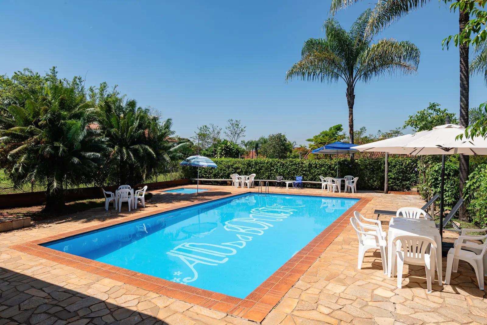 Piscina adulto com o logo do hotel e a piscina infantil ao fundo