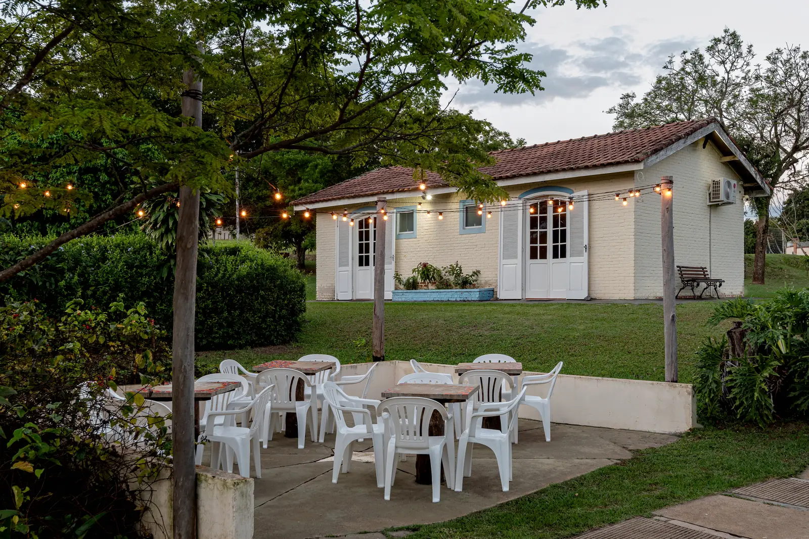 Varal de luzes acesas sobre as mesas do espaço de convivência junto ao jardim